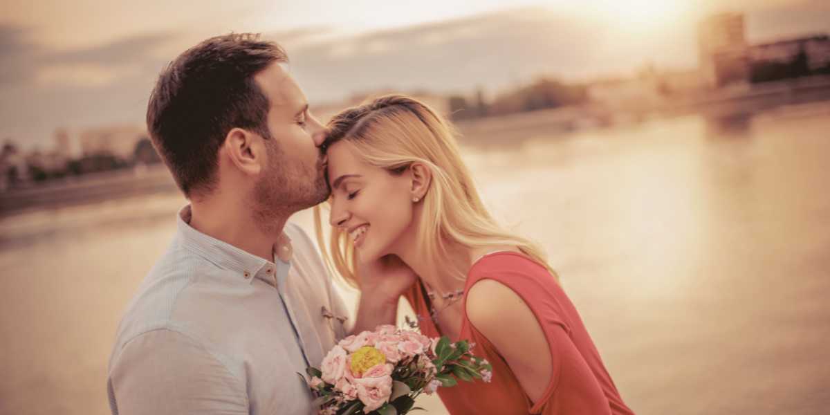 Couple embracing, woman holding flowers next to ocean