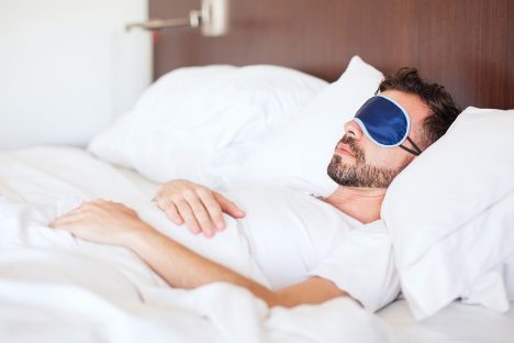 Portrait of a young man with a beard using a sleep mask to get some rest in a hotel